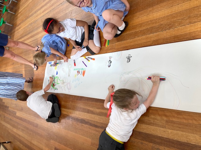 a long roll of paper on the floor with 5 children around it drawing on it